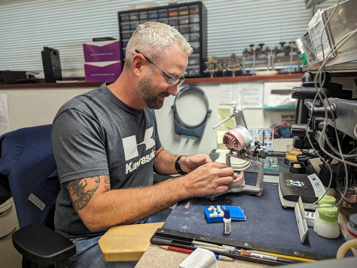 Técnico em laboratório conferindo adaptação e acabamento de prótese dental